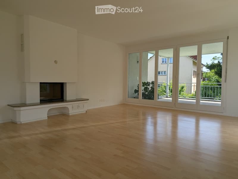 Empty room with wooden flooring, white walls, and a built-in fireplace. Large sliding glass doors lead to a balcony or outdoor area.