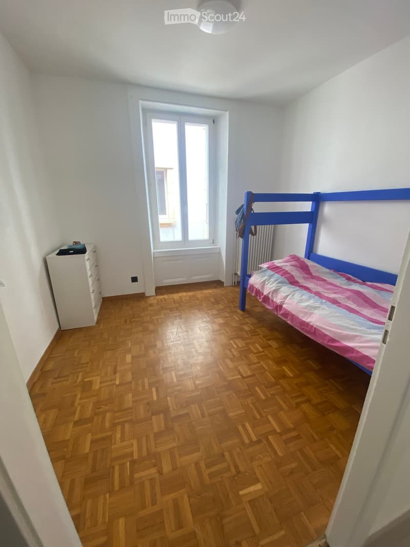 Bedroom with wooden herringbone flooring, a blue bunk bed with pink and white bedding, a white dresser, and a radiator under the window.
