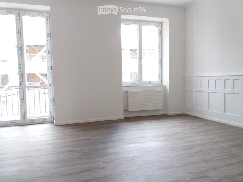 Empty room with light wooden flooring, white walls, and large windows with protective film. No furniture or equipment present.