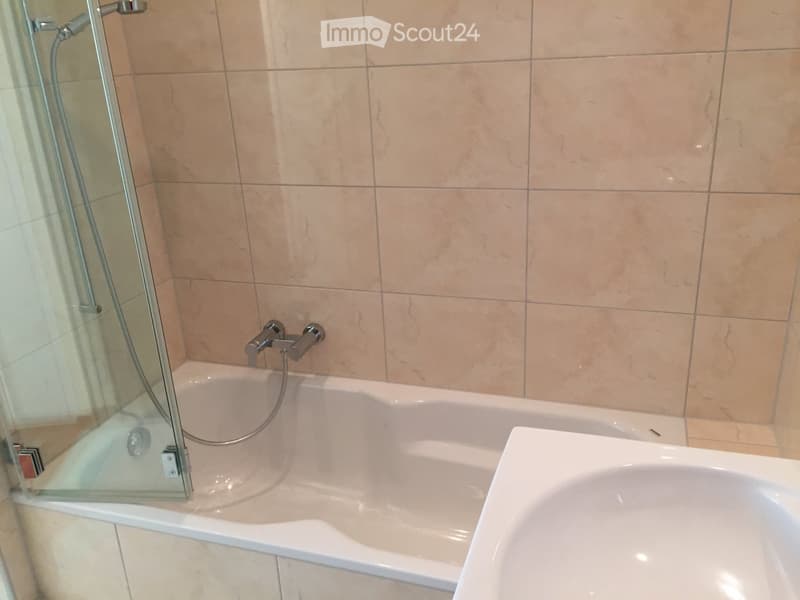 Modern bathroom with a bathtub, glass shower enclosure, and a separate sink. Beige tiles and chrome fixtures.