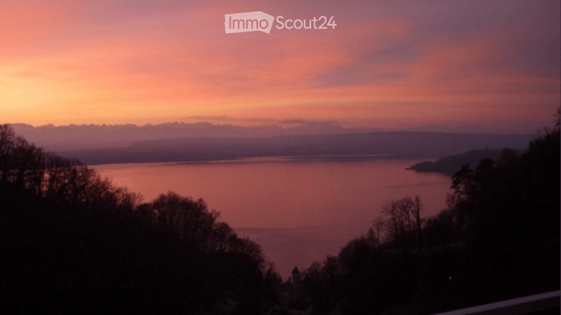 A scenic view of a lake at sunset, with a colorful sky and distant mountains.