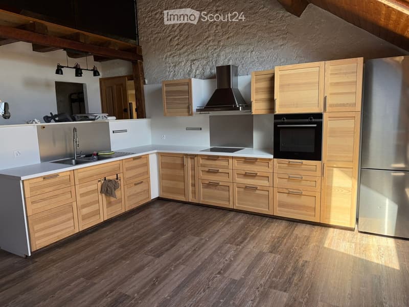 Modern kitchen with light wooden cabinets, stainless steel appliances, and a central island. Features a sink, oven, refrigerator, and range hood.