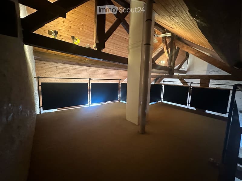 An open, spacious hallway with wooden beams and exposed wooden ceiling, featuring a metal railing and a polished concrete floor.
