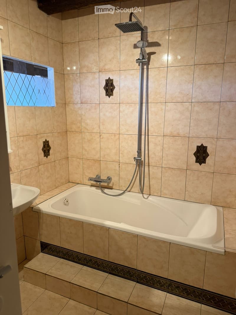 Bathroom with beige tiled walls and floor, a bathtub with a handheld showerhead, a sink, and decorative wall tiles.
