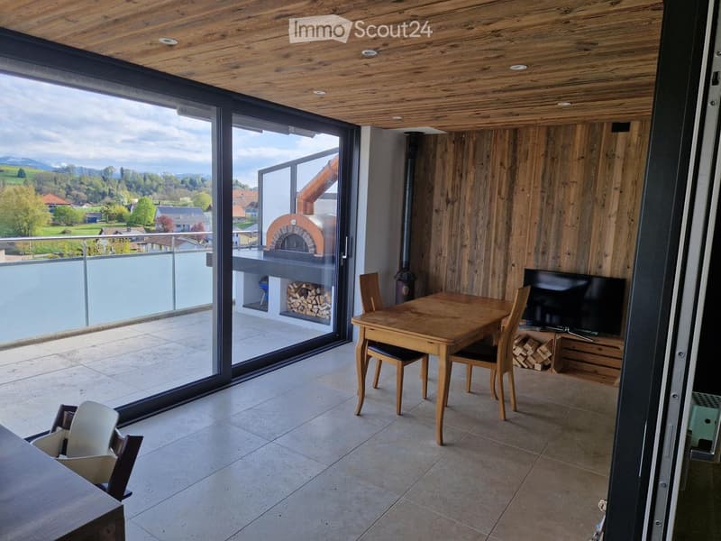 Modern dining area with wooden table, chairs, and TV, large sliding glass doors leading to a balcony with scenic mountain view.