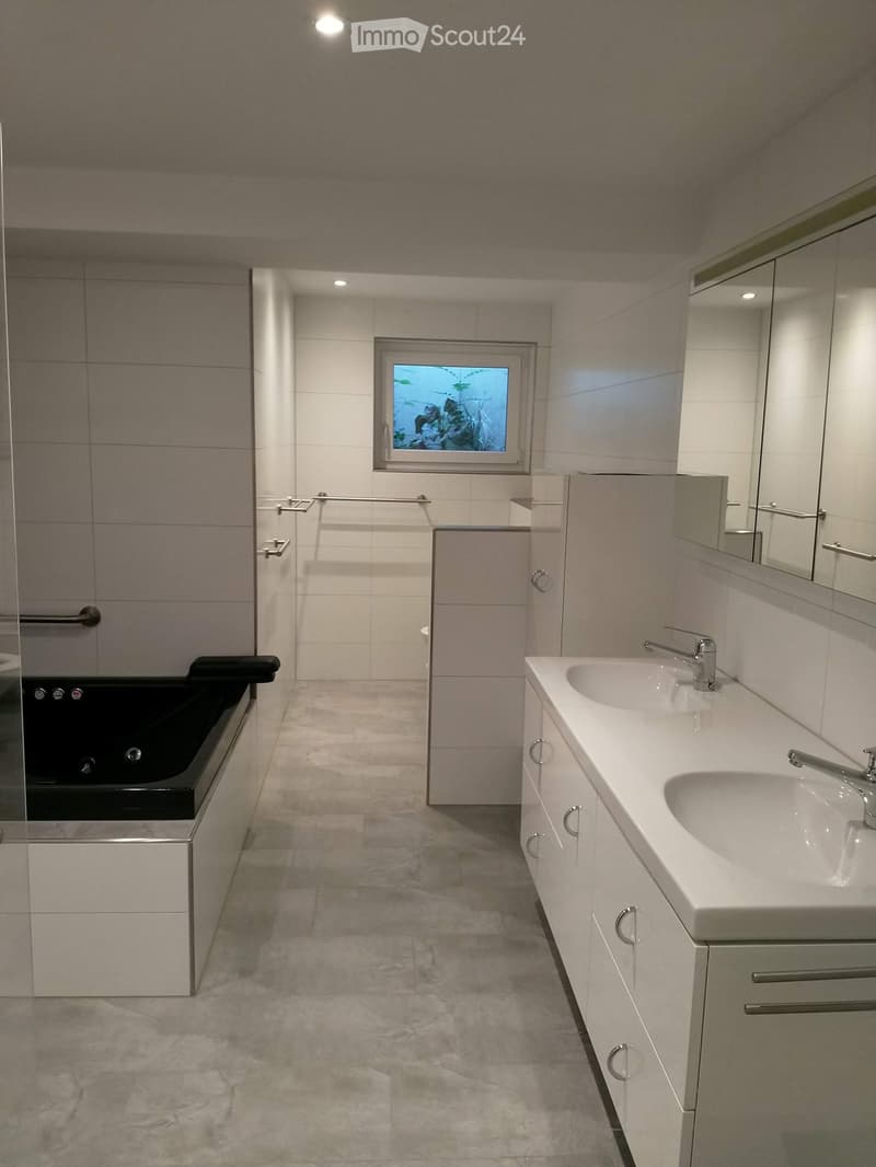 Modern bathroom with a double sink vanity, mirrored cabinet, bathtub, and a window with a view of greenery.