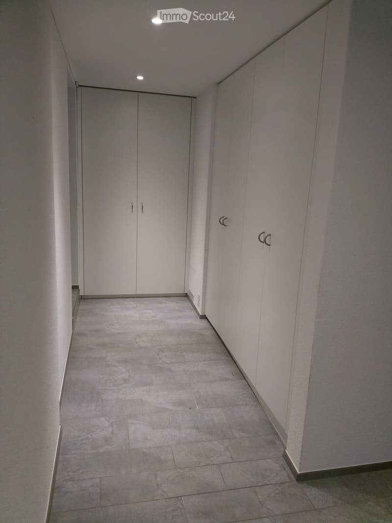 Clean, modern hallway with white walls, grey tiled floor, and built-in white storage units with silver handles.