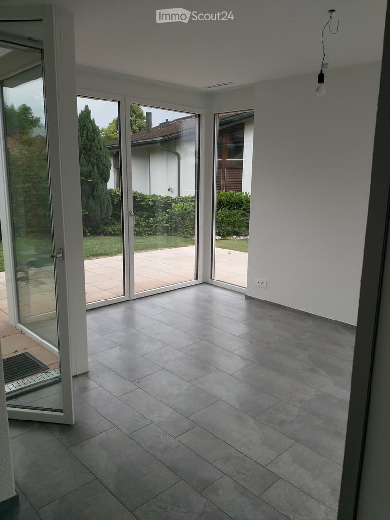 Empty room with large sliding glass doors leading to a patio and garden, tiled floor, white walls, and visible electrical outlets.