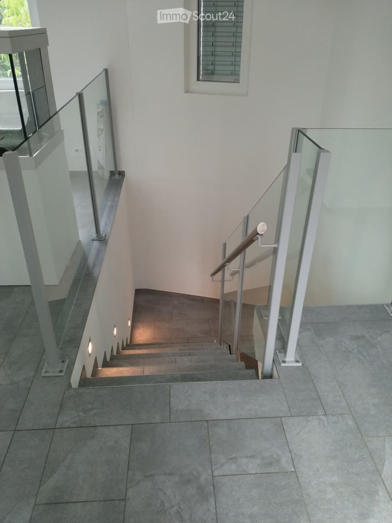 Modern staircase with glass railings, metal balusters, and built-in lighting, leading upwards with a window at the top.
