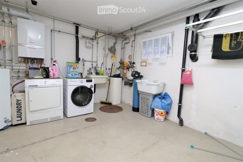 a basement room with white washer, dryer, sink, trash bins, baskets, laundry bags, water heater