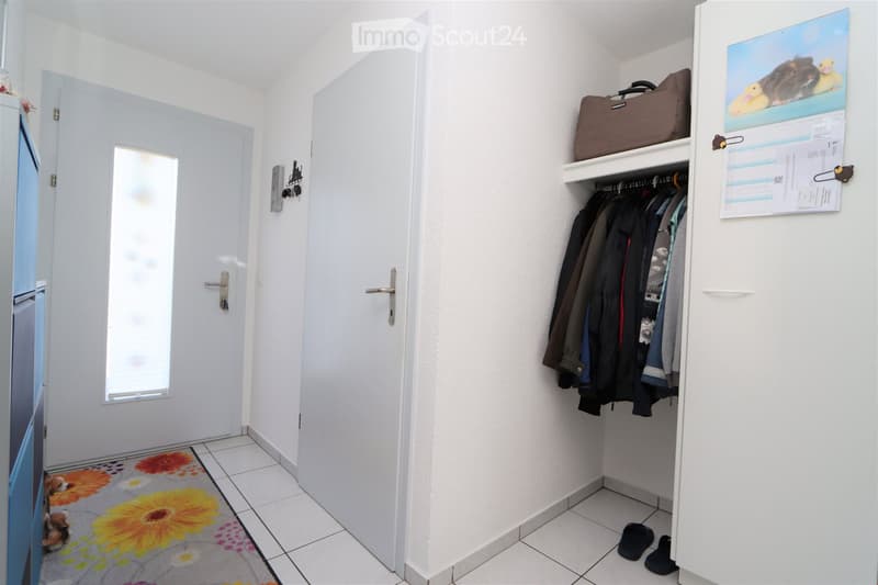 white tiled floor, white wall, closet with clothes and bags, rug with flowers, entrance doors