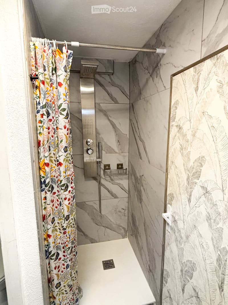 Modern shower area with marble tiles, floral shower curtain, and a sleek showerhead with control panel.