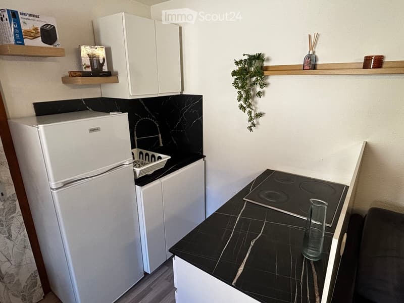 Modern kitchen with white cabinets, black marble countertops, induction stove, refrigerator, and wooden shelves with decorative items.