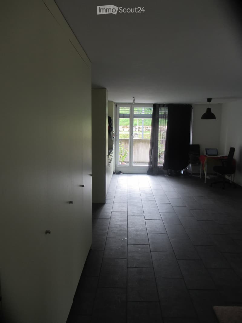 Furnished Room. Bright room with tiled floor, large window with dark curtains, small table with laptop and chair, and a built-in closet on the left side.