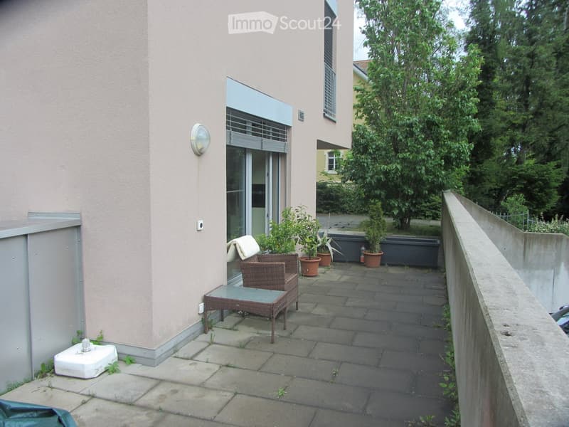 Balcony / Terrace. Balcony with a small seating area, including a table and a wicker chair, surrounded by potted plants and a low wall.