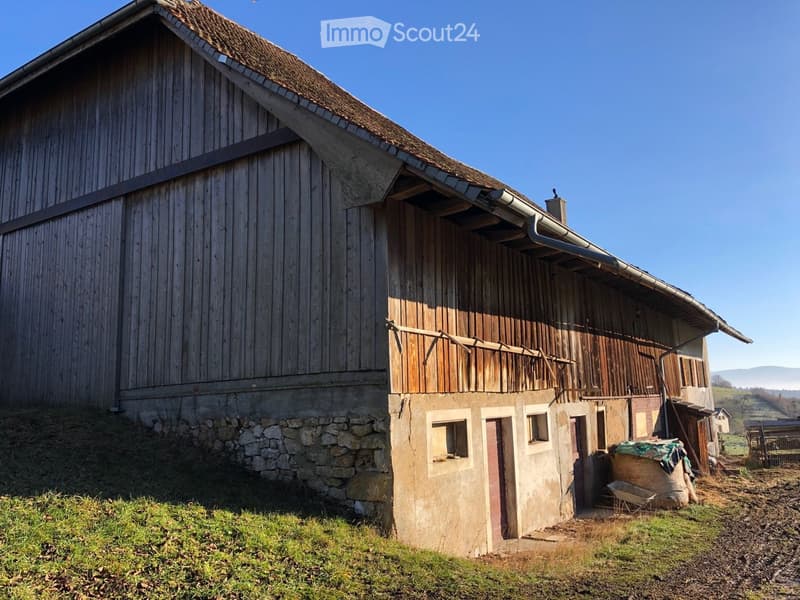 Old wooden barn with stone foundation, rustic exterior, large windows, pitched roof, located in rural area