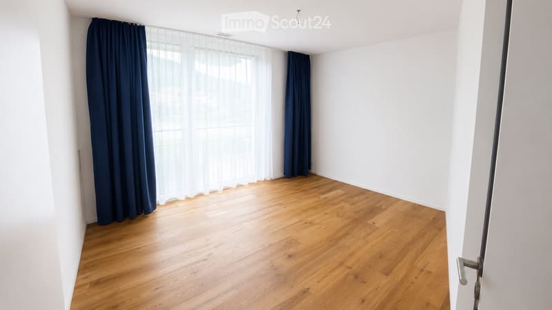 Empty room with wooden flooring, white walls, and large windows with dark blue curtains.