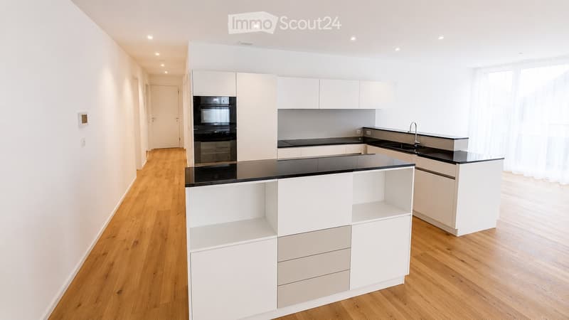Modern kitchen with white cabinets, black countertops, and a central island. Features include an oven, sink, and faucet.