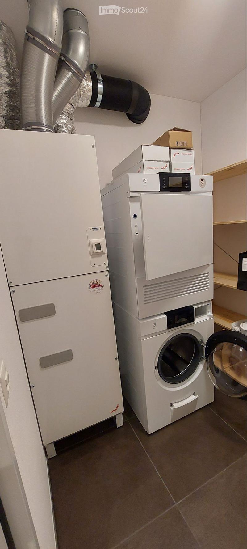 A small utility room with a washing machine, dishwasher, and control panel, featuring a tiled floor and white walls.