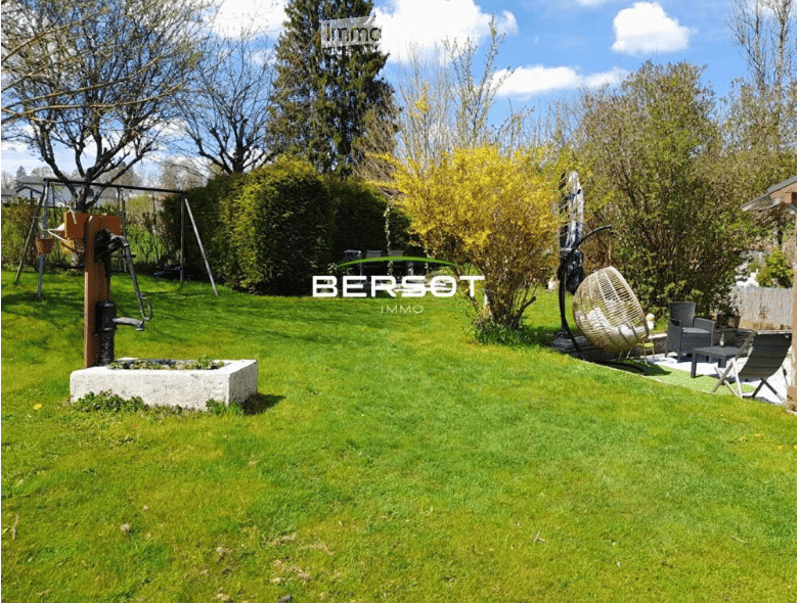 Well-maintained garden with green lawn, trimmed hedges, a swing set, a water fountain, and outdoor seating area with chairs and a table.