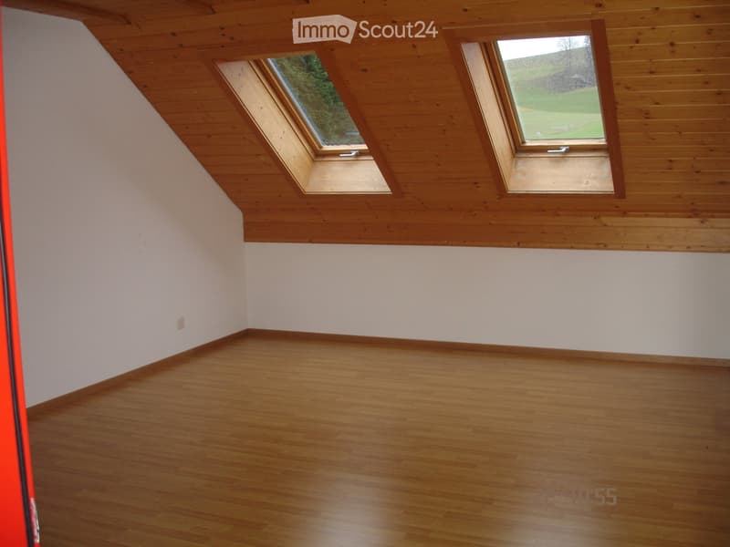 Empty room with wooden flooring and slanted wooden ceiling, featuring two skylight windows offering a view of the outdoors.
