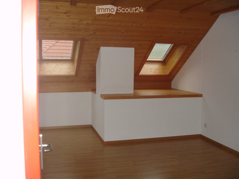 Empty attic room with wooden ceiling, wooden floor, white walls, and skylight windows.