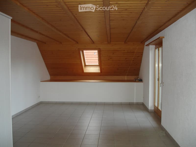 Empty attic room with wooden slanted ceiling, tiled floor, and a small skylight window.