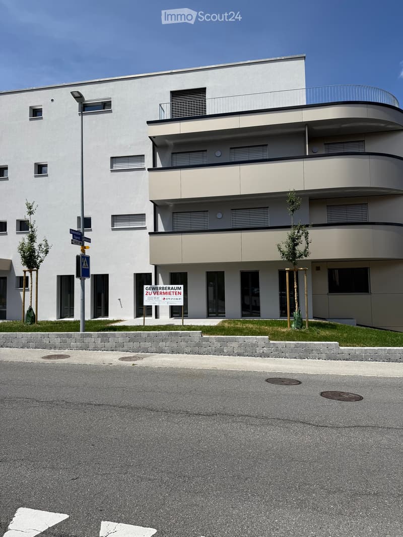 Modern two-story building with white facade, large windows, and a curved balcony on the upper level.