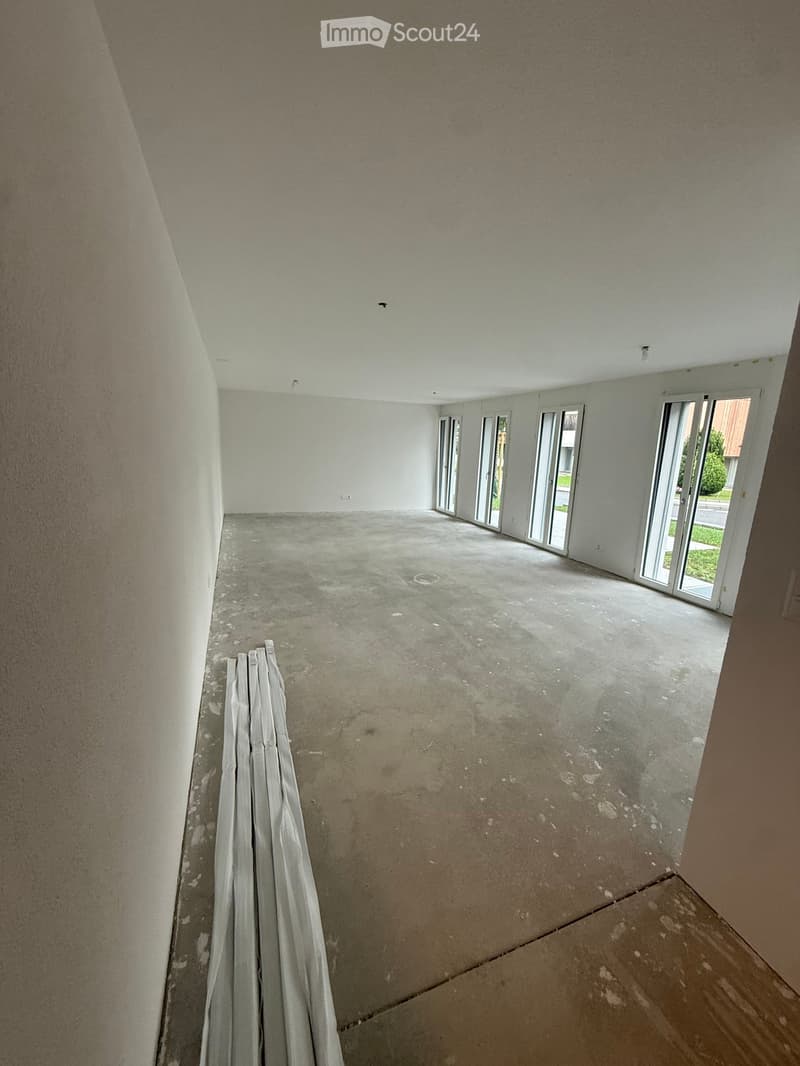 Empty room with unfinished concrete floor and white walls, featuring large glass sliding doors leading to an outdoor area.
