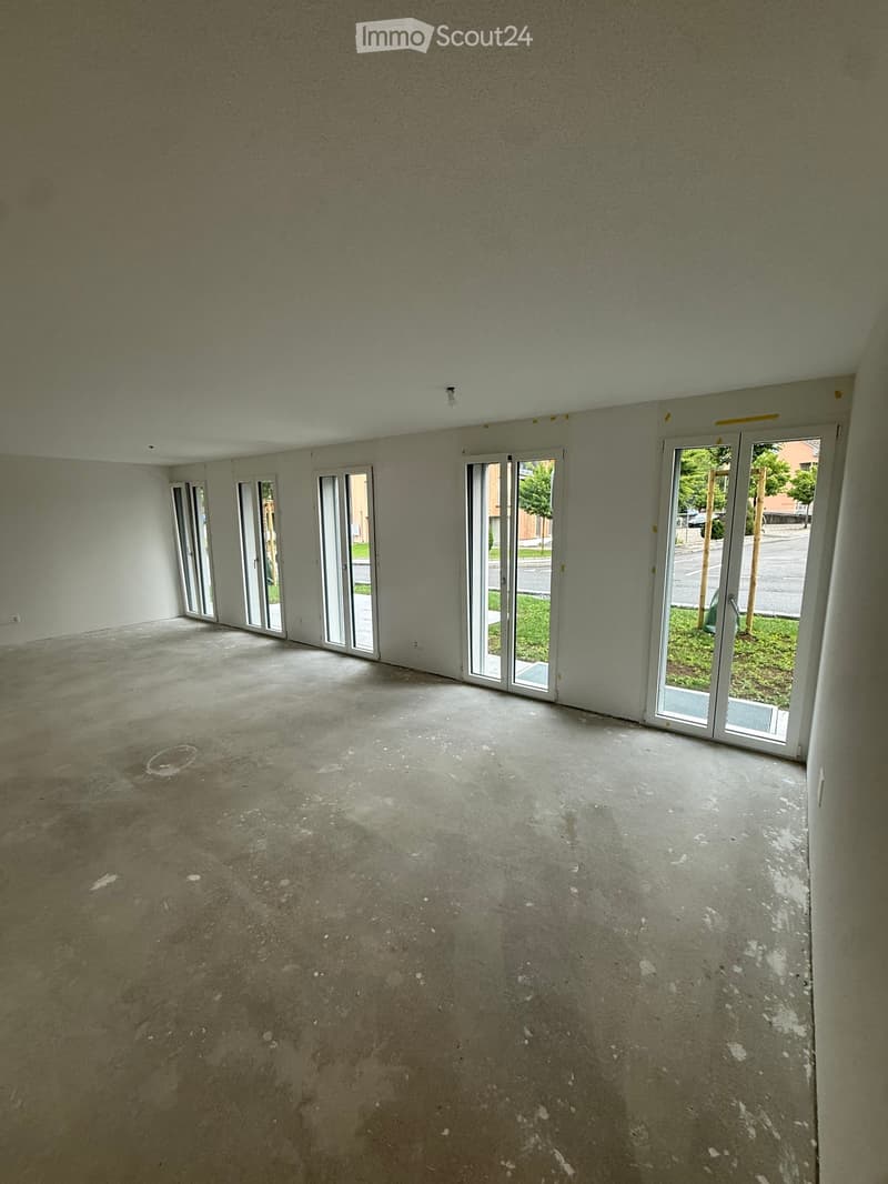 Empty room with bare walls and concrete floor, multiple large sliding glass doors leading to outdoor area.