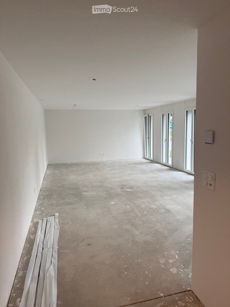 Empty room with white walls, concrete floor, and large sliding glass doors leading outside.