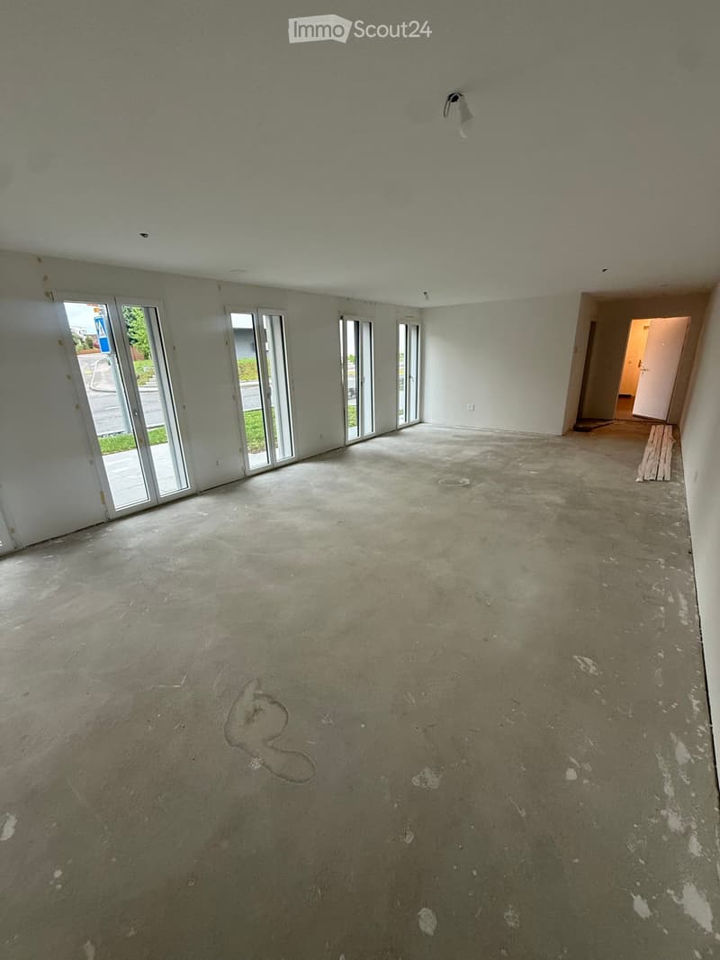 Empty room with bare walls and concrete floor, featuring large glass sliding doors leading to an outdoor area and a doorway to another room.