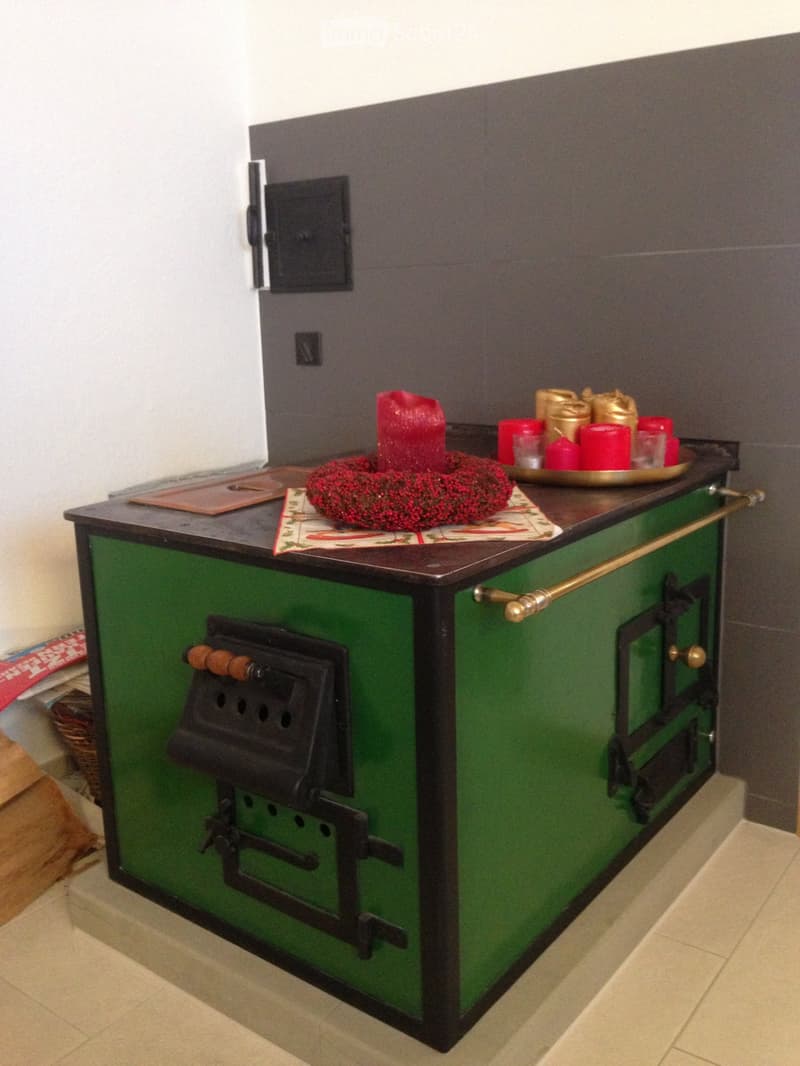 A green stove with a black top, decorated with a red wreath, candles, and a tray of golden items.