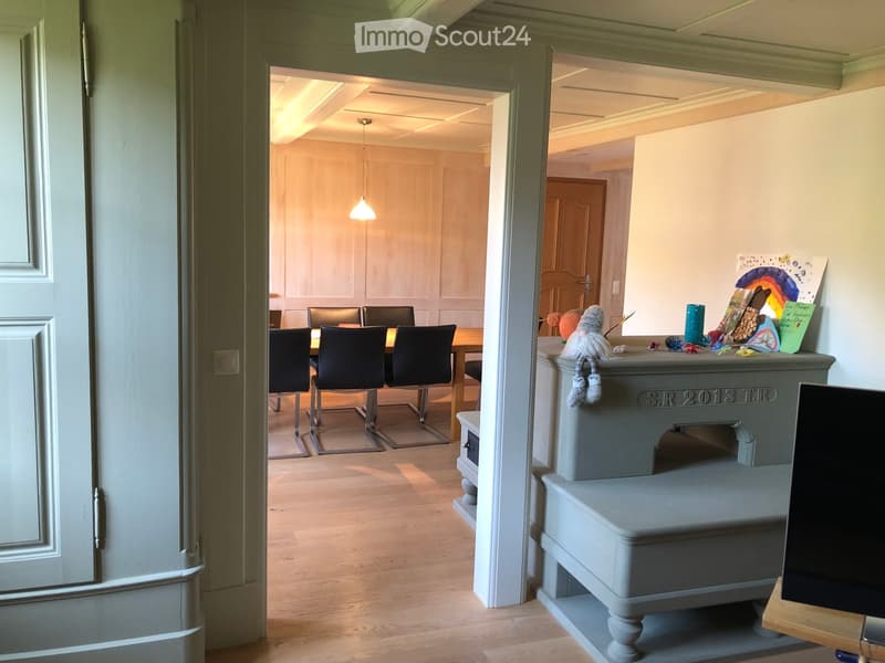 A well-lit hallway leads to a dining area with a table and chairs, and a small sitting area with a stool and decorative items.