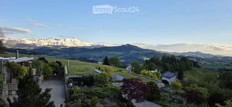 Garden / Outdoor Area. A panoramic view of a lush garden area with a modern building, surrounded by rolling hills and snow-capped mountains in the background.