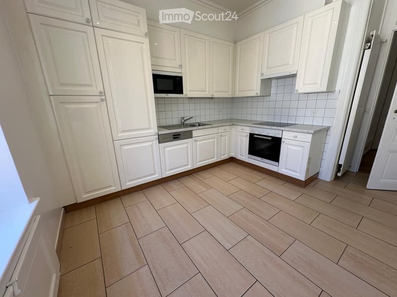 Modern kitchen with white cabinets, tiled backsplash, and light wood flooring. Features a microwave, dishwasher, and oven.