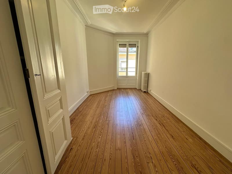 Empty hallway with wooden flooring, white walls, and a window at the end. A radiator is visible on the right side.