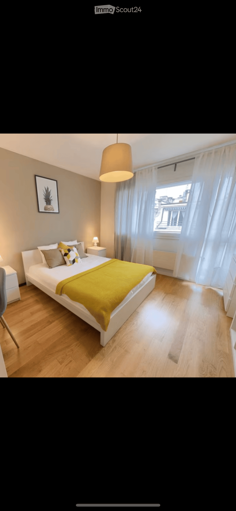 Modern bedroom with a white bed, yellow blanket, nightstand, chair, and large window with curtains.