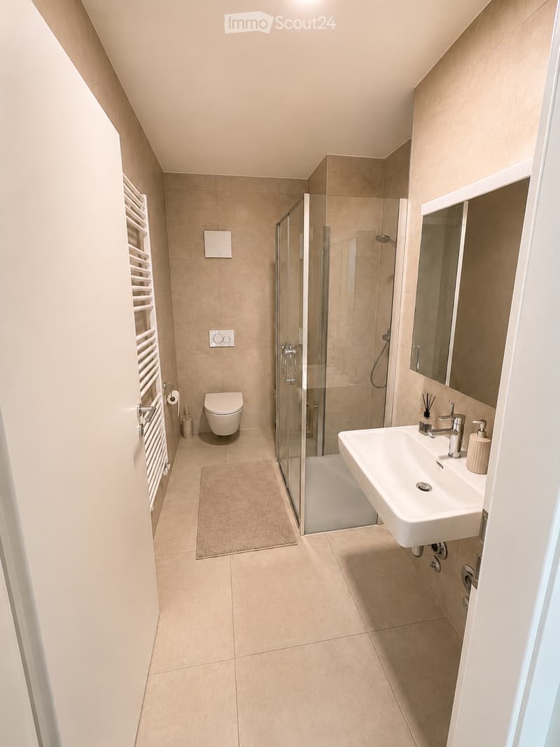 Modern bathroom with beige tiles, a white sink, a toilet, a glass-enclosed shower, and a towel rack.