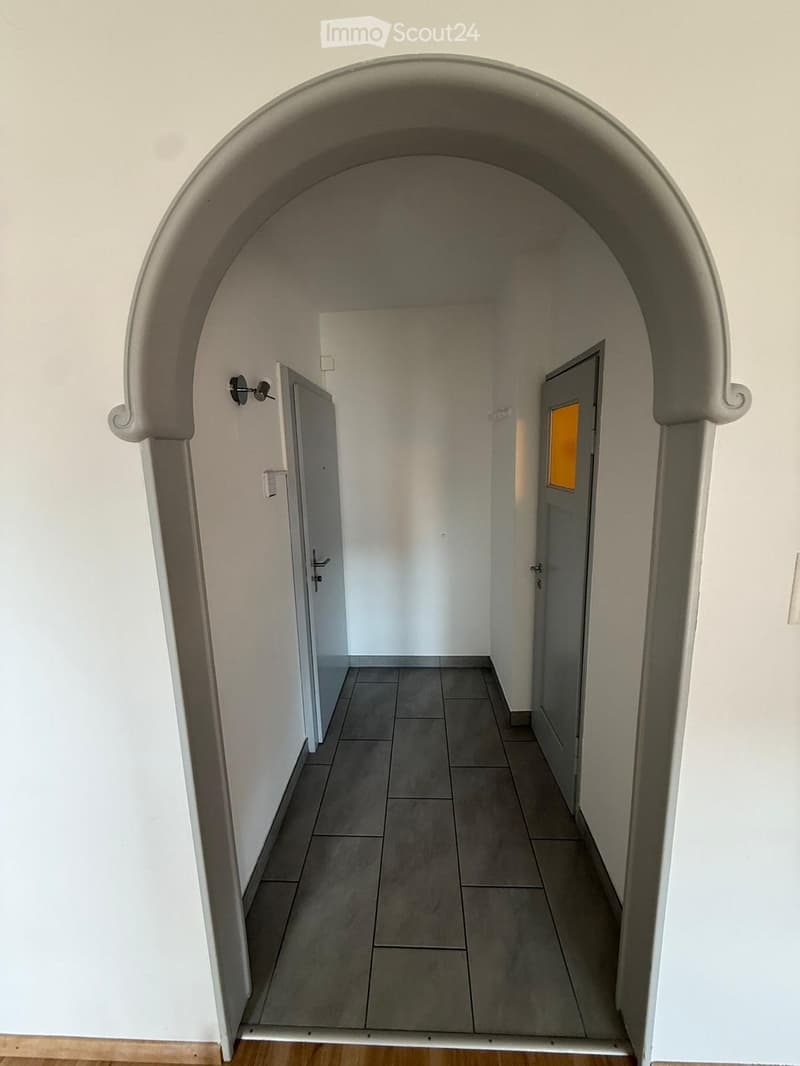 Empty hallway with tiled floor, white walls, and two doors at the end.