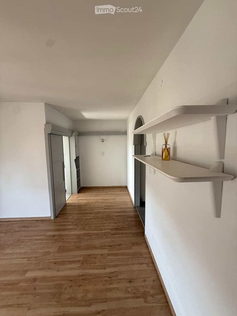 Empty hallway with wooden flooring, white walls, and built-in shelving on one side.