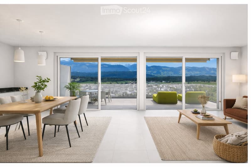Open-plan living and dining area with large windows offering a scenic mountain view. Features a wooden dining table with chairs, a brown sofa, a wooden coffee table, and decorative items including a vase with plants and books.