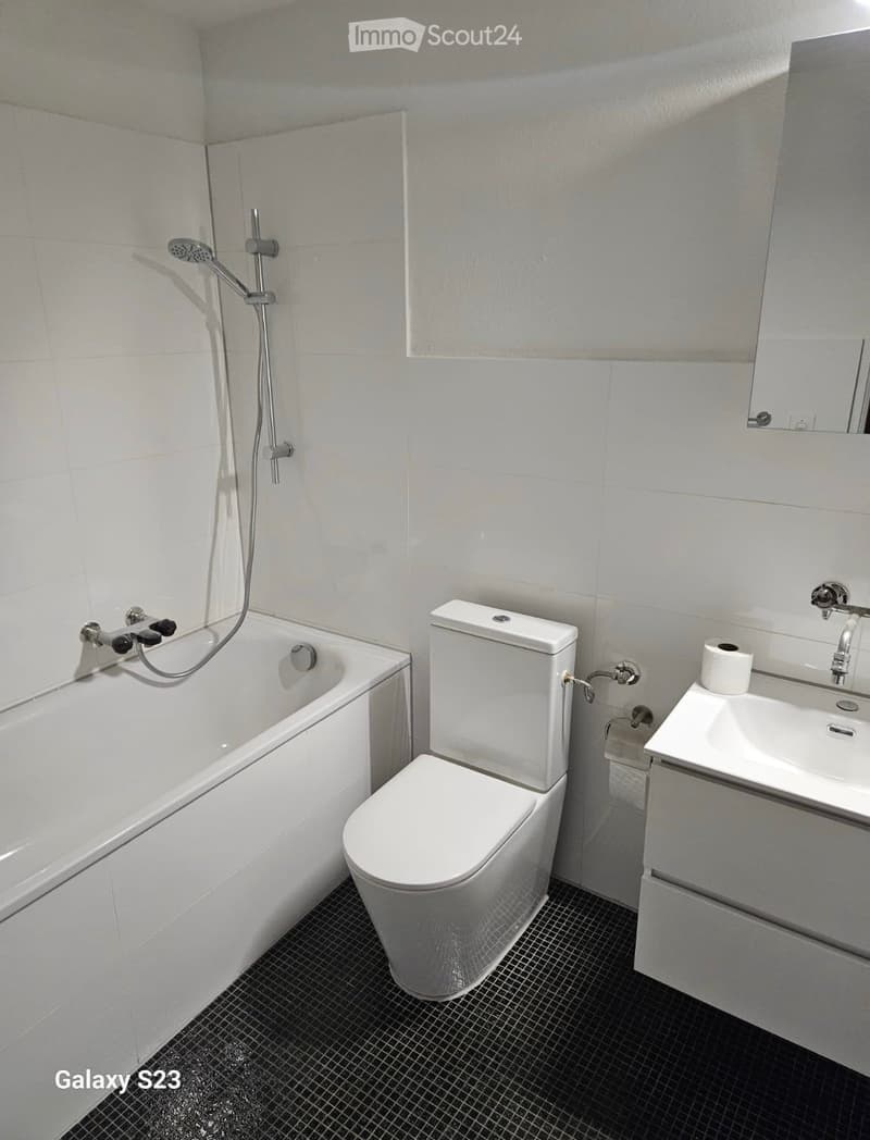 Modern bathroom with white tiles, a bathtub, toilet, sink, and showerhead.