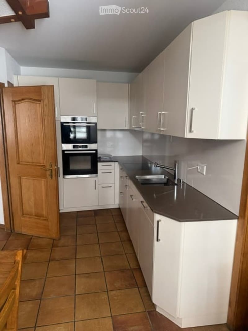 Modern kitchen with white cabinets, stainless steel oven, dark countertop, and tiled floor.