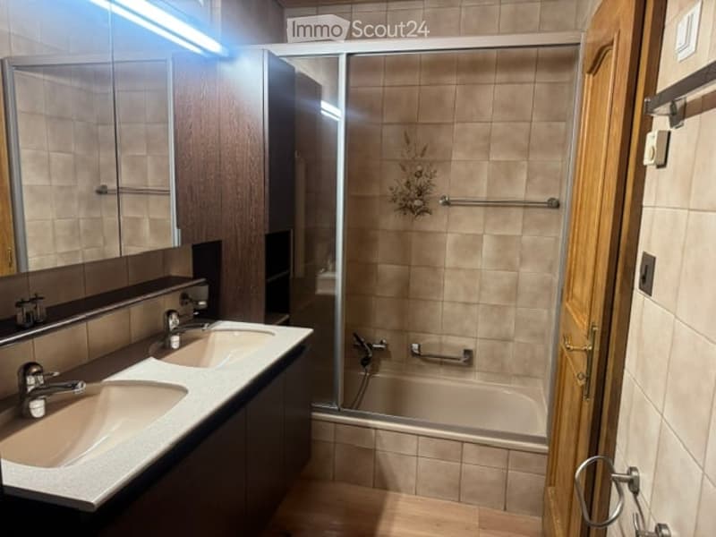 Modern bathroom with double sinks, a large mirror, a bathtub with a glass shower enclosure, and tiled walls.
