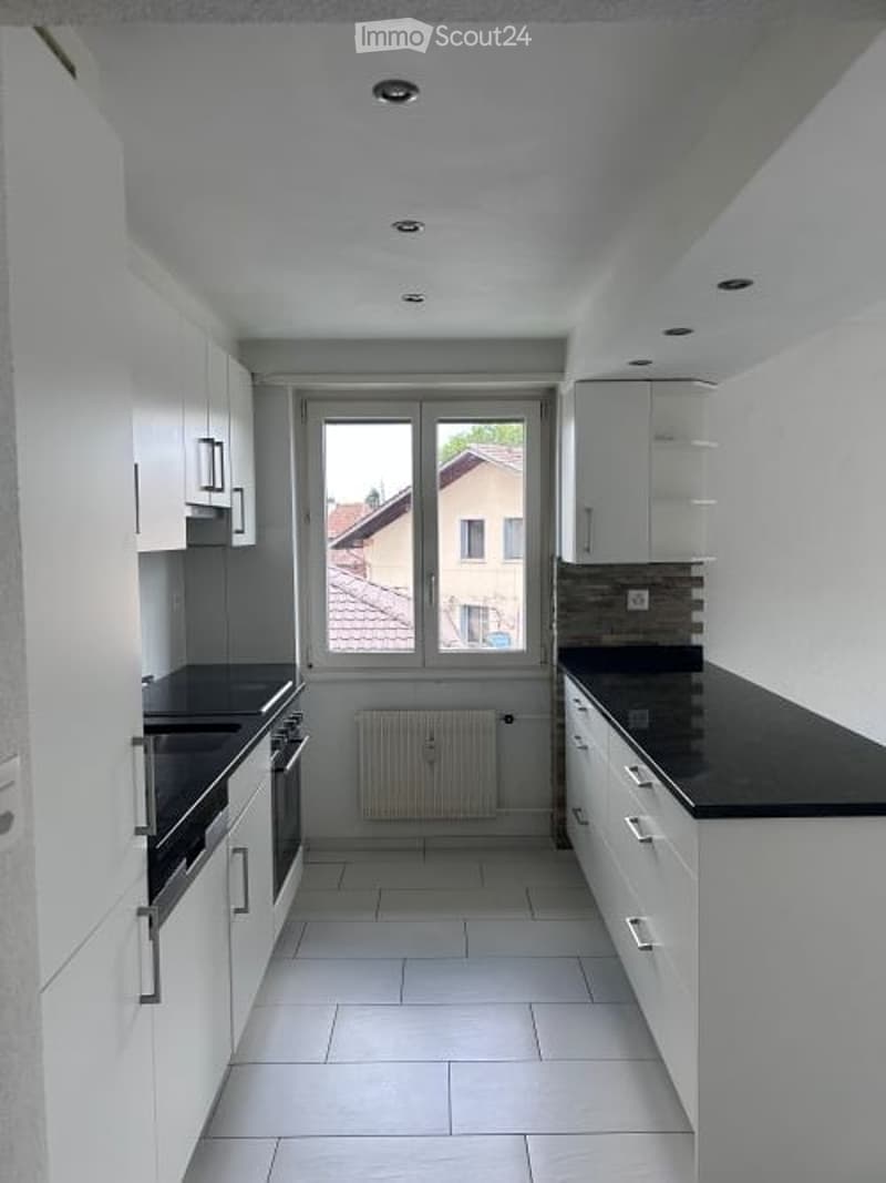 Modern kitchen with white cabinets, black countertops, and a large window offering a view of the street.