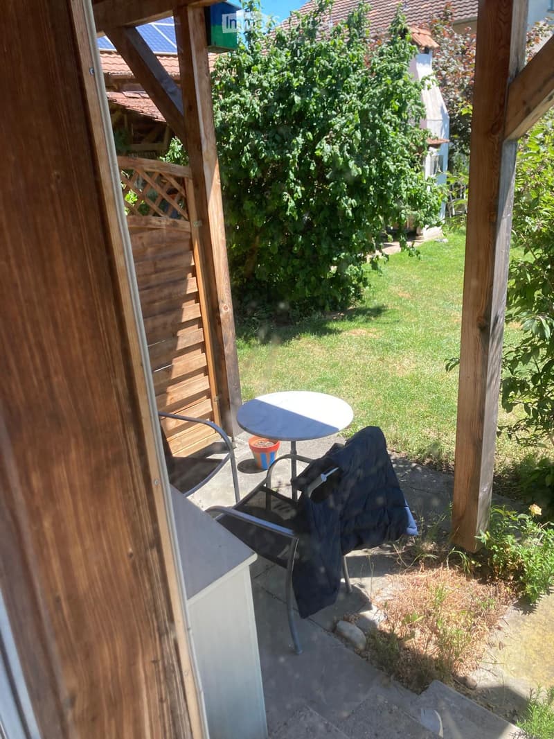 Balcony with a round table, a chair, and a small potted plant, overlooking a grassy garden area.