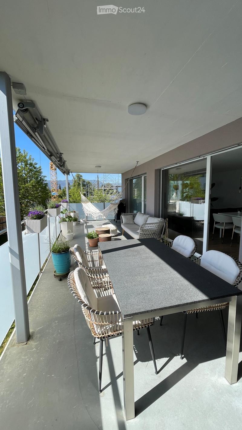 Balcony with a modern outdoor dining setup, including a table, chairs, a sofa, a hammock, and potted plants.
