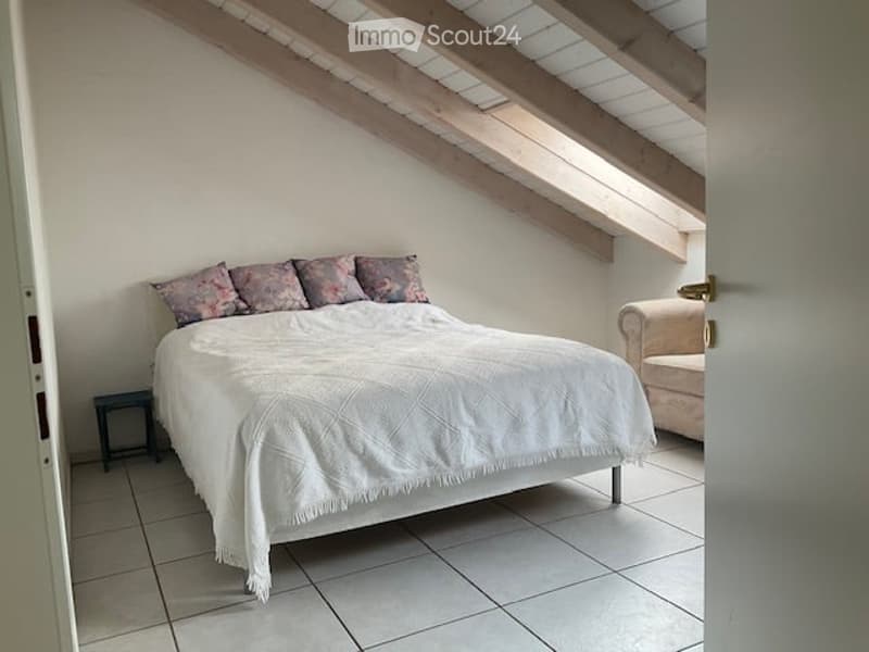 Cozy bedroom with a large bed, white bedding, decorative pillows, a nightstand, and a small sofa in the corner.