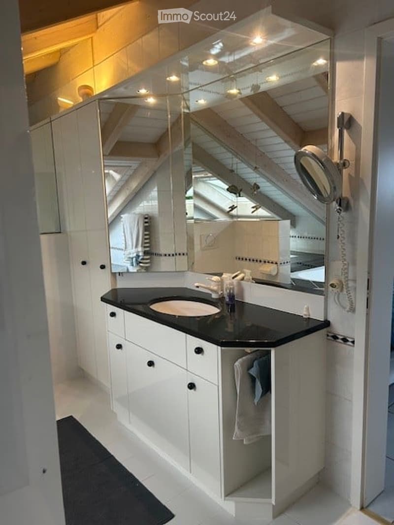 Modern bathroom with white cabinets, black countertop, large mirror, and built-in shelving. Features a sleek sink and towel hanging on the side.